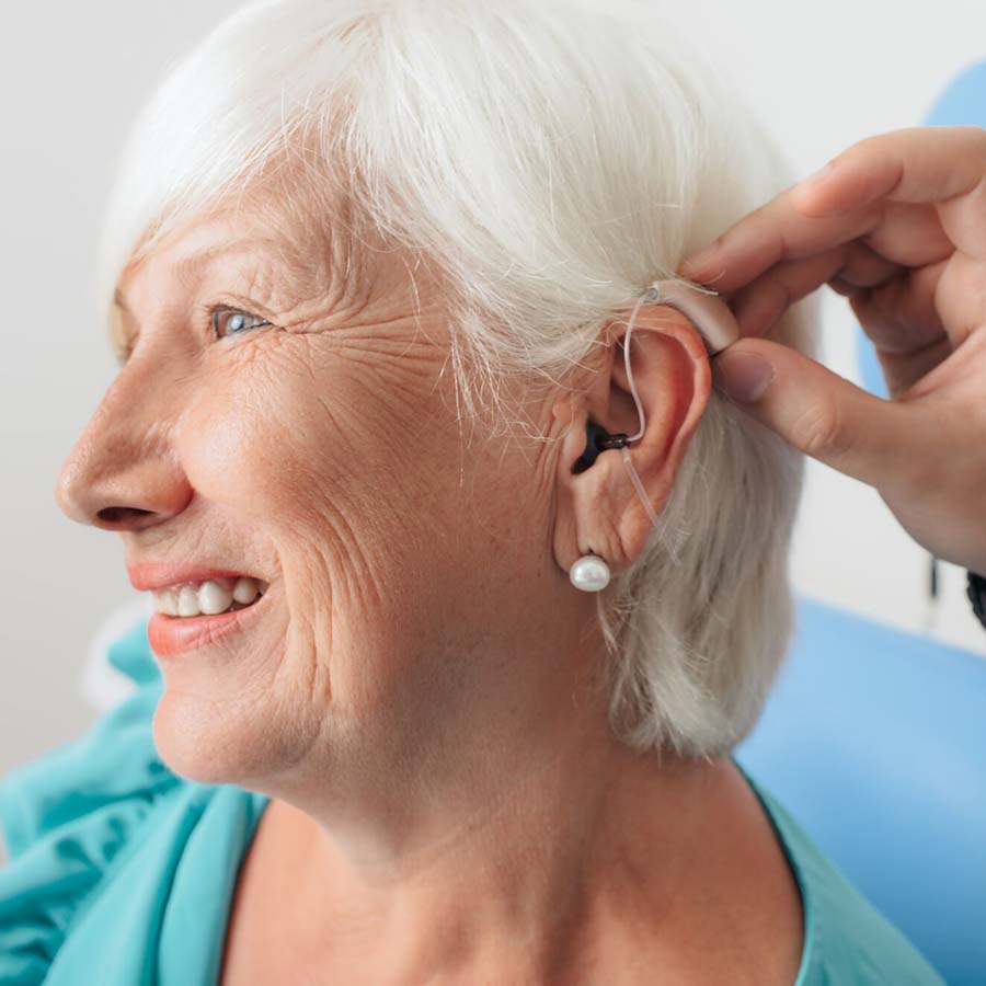 an elderly woman putting on a hearing aid